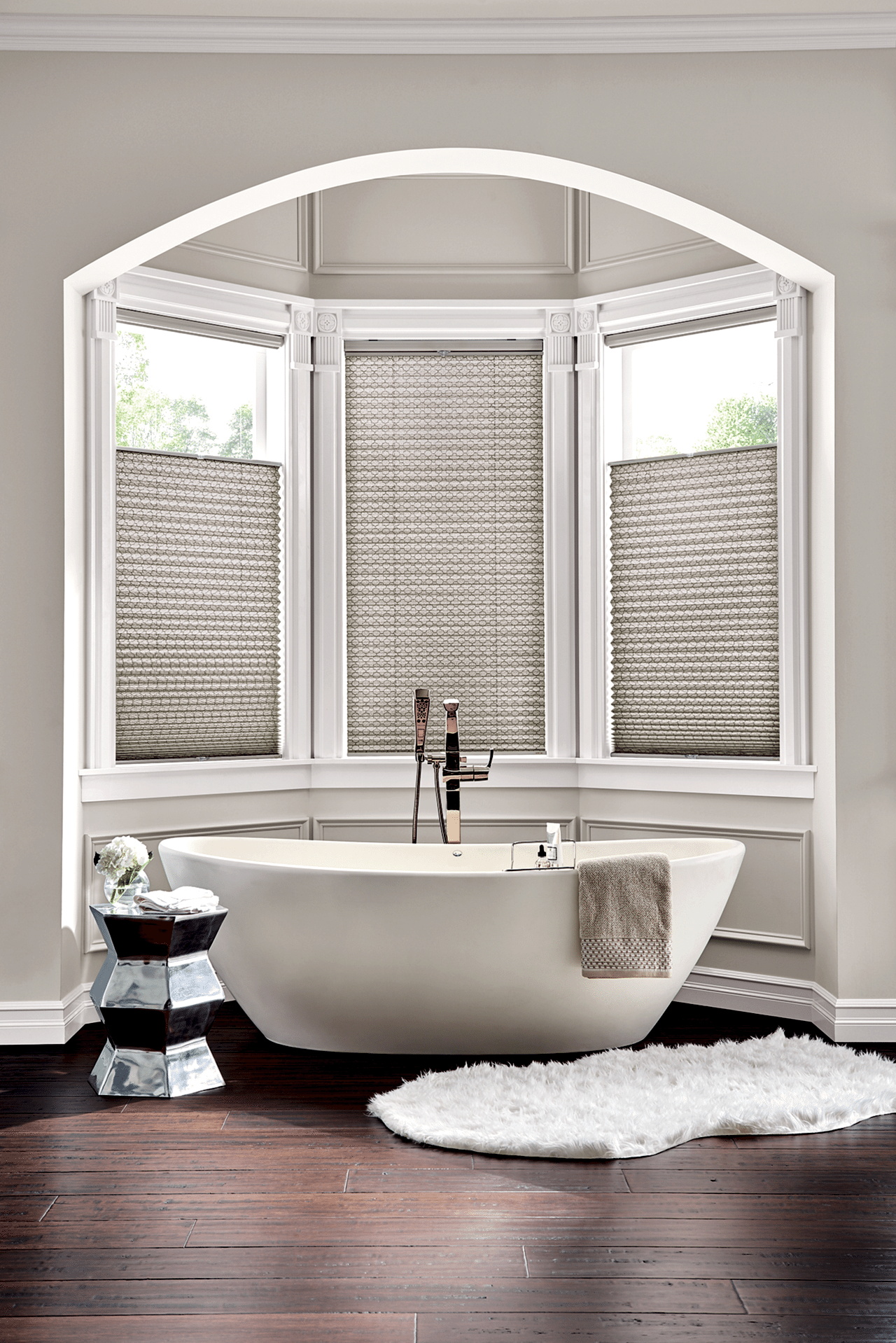 Bathroom with a freestanding tub, white rug, and bay windows fitted with top-down pleated shades.