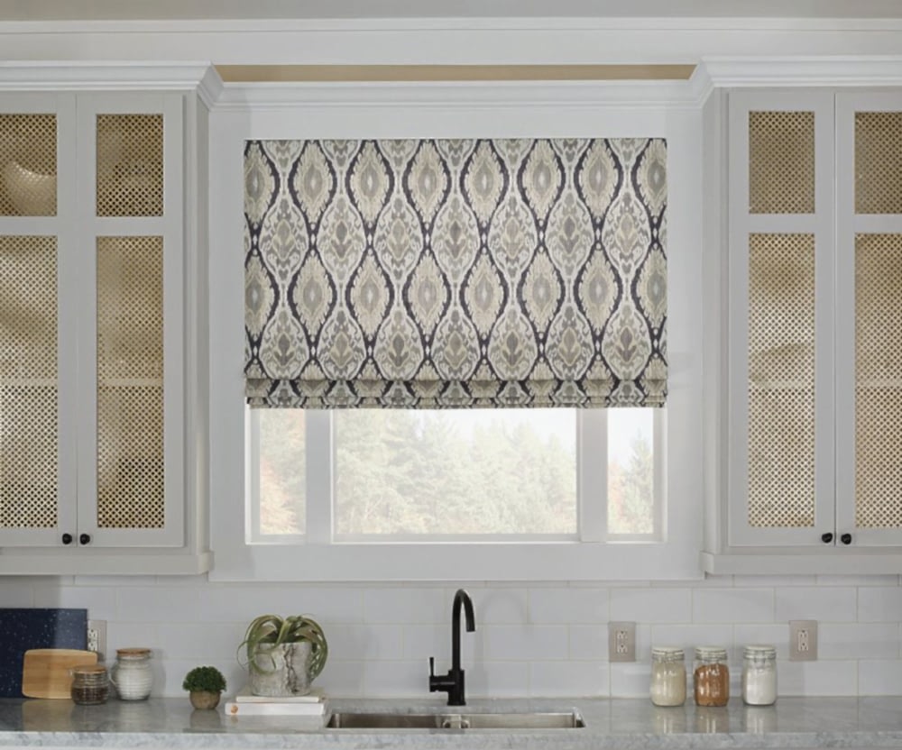 Roman shades above a sink filtering in light in a kitchen.