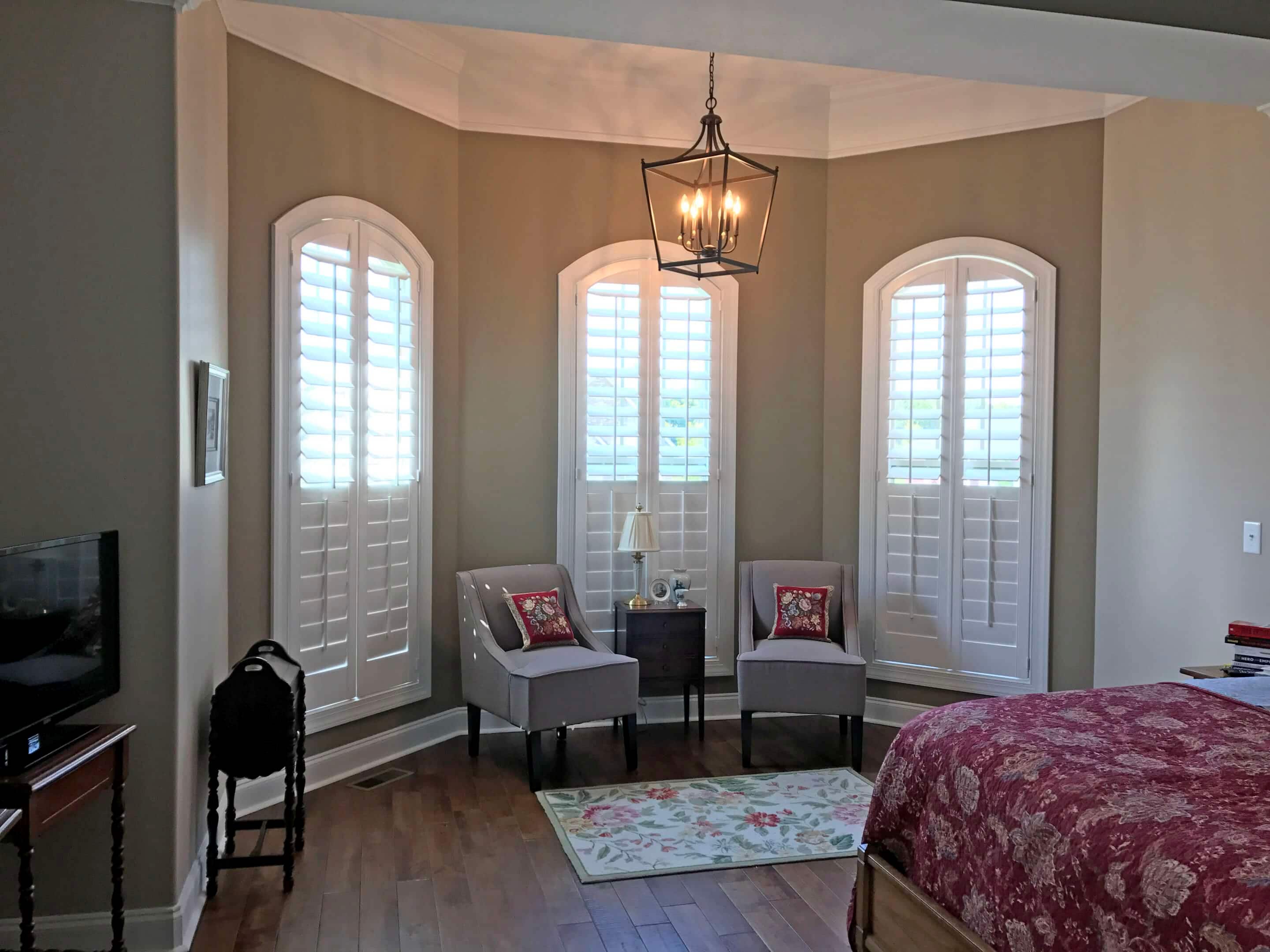 Bay window seating area with three tall arched plantation shutters